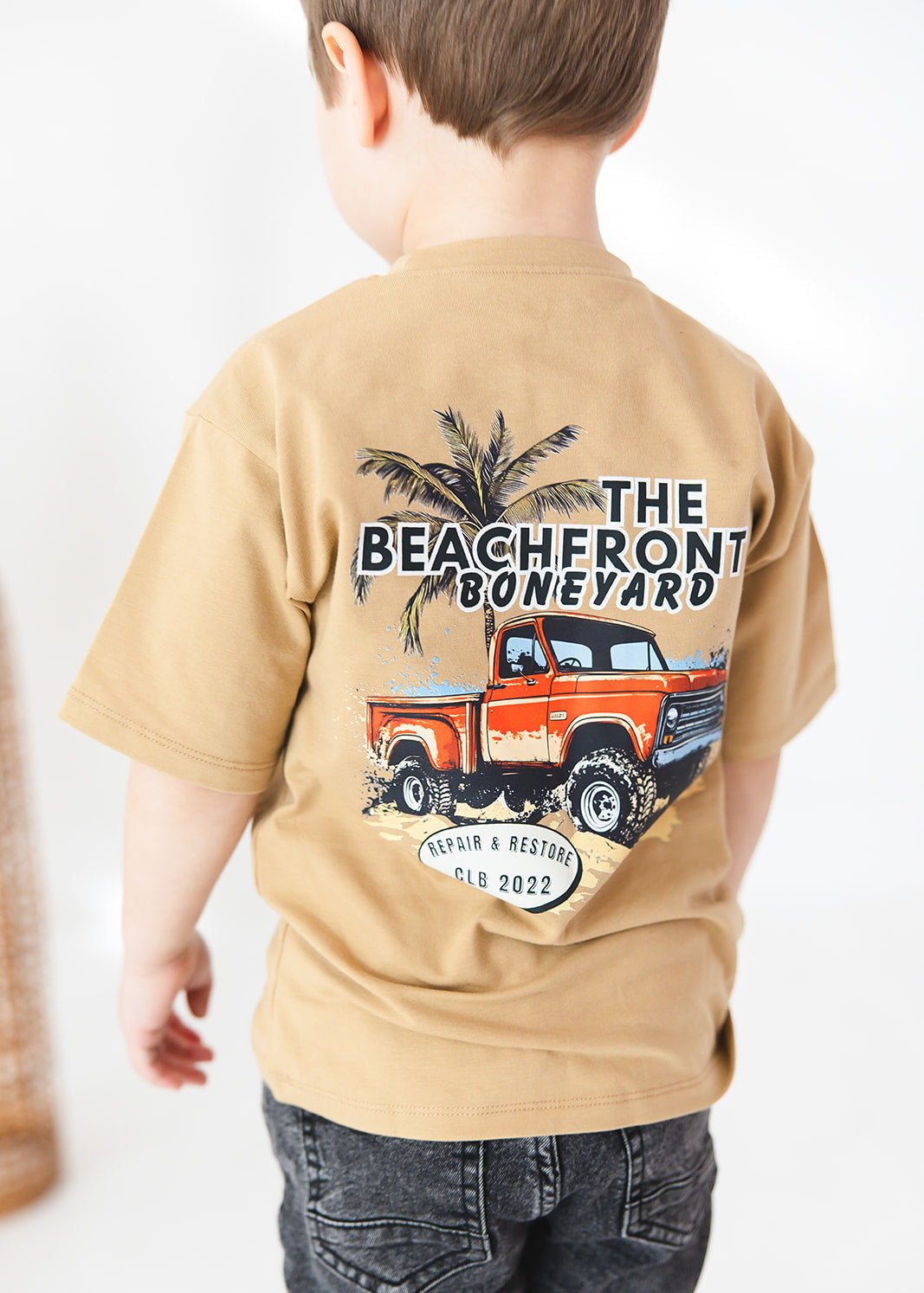 Skater style t-shirt for baby, toddler and little boys. Beige cotton shirt with a truck and palm tree graphic on the back. Soft, stretchy and thick fabric that is perfect for play with Charlie Lou Baby word logo on front.