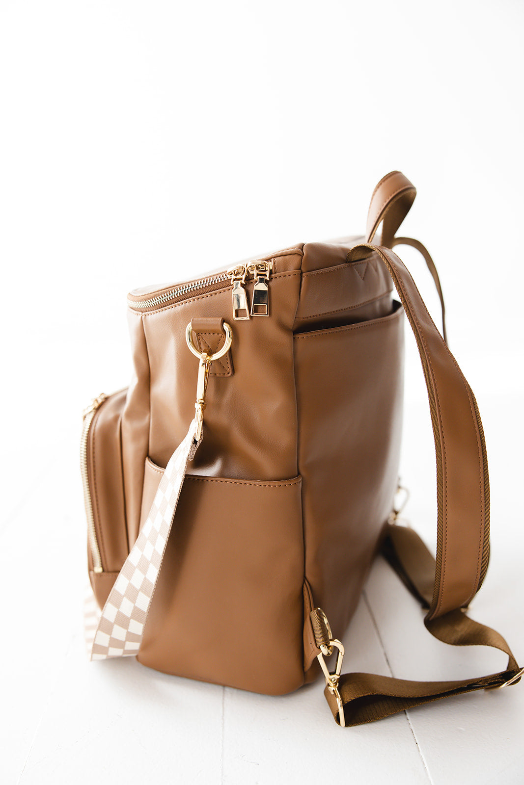Brown faux leather large diaper bag with checkered cross body strap, insulated bottle pockets, changing mat, and stroller straps.
