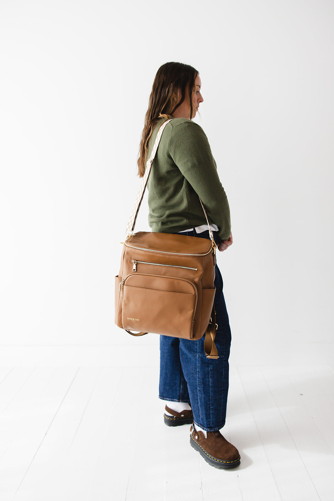 Brown faux leather large diaper bag with checkered cross body strap, insulated bottle pockets, changing mat, and stroller straps.