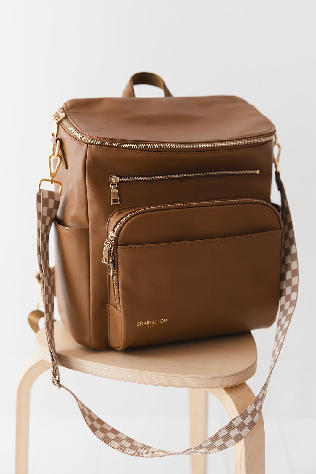 Brown faux leather large diaper bag with checkered cross body strap, insulated bottle pockets, changing mat, and stroller straps.