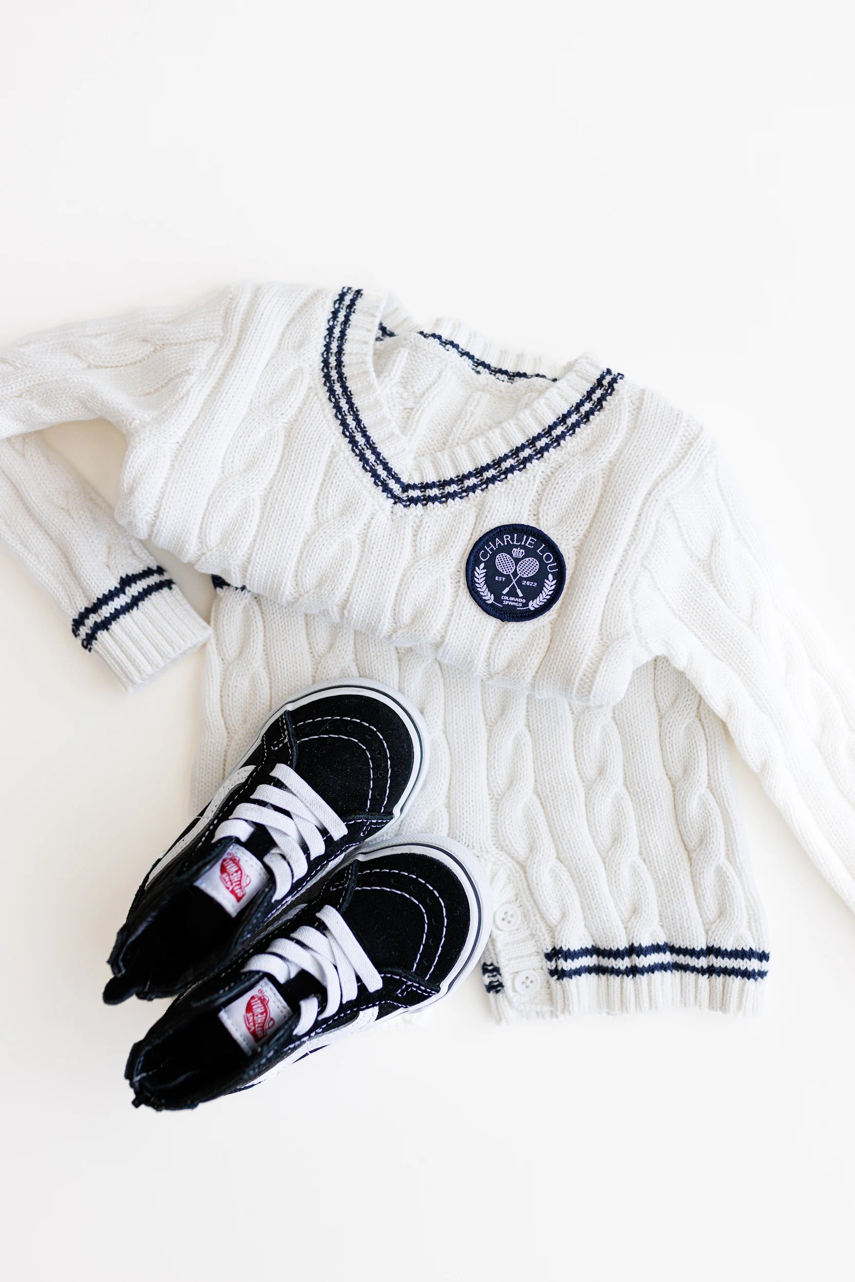 Gender neutral varsity sweater romper in cream and navy blue colors made from chain knit cotton for baby boys and baby girls as well as toddlers.