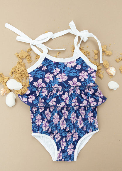 Bathing suit for baby, toddler and little girls. One piece swim suit with pink florals and blue background that is ribbed fabric on the top and smocked on the bottom with adjustable straps that tie into bows.