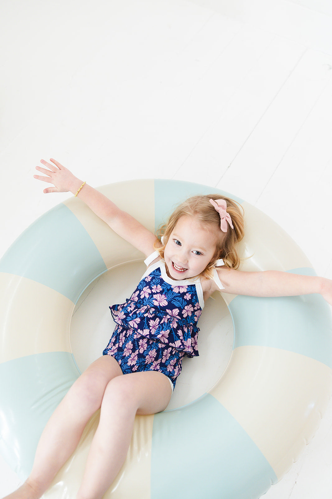 Bathing suit for baby, toddler and little girls. One piece swim suit with pink florals and blue background that is ribbed fabric on the top and smocked on the bottom with adjustable straps that tie into bows.