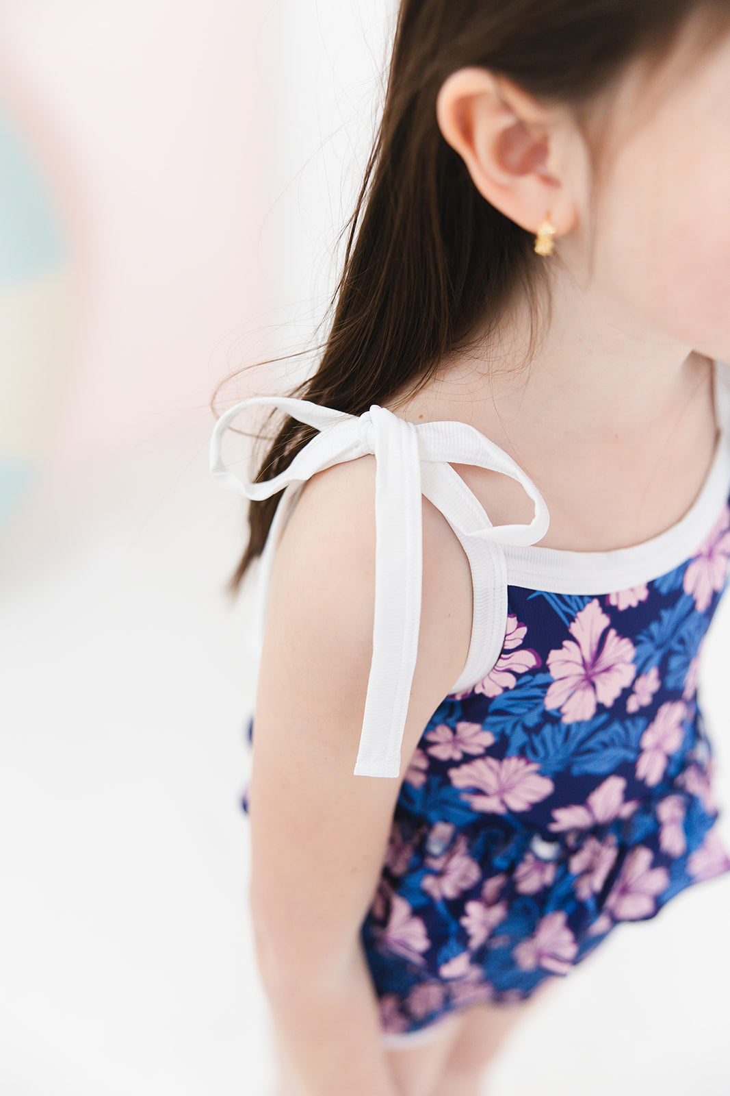 Bathing suit for baby, toddler and little girls. One piece swim suit with pink florals and blue background that is ribbed fabric on the top and smocked on the bottom with adjustable straps that tie into bows.