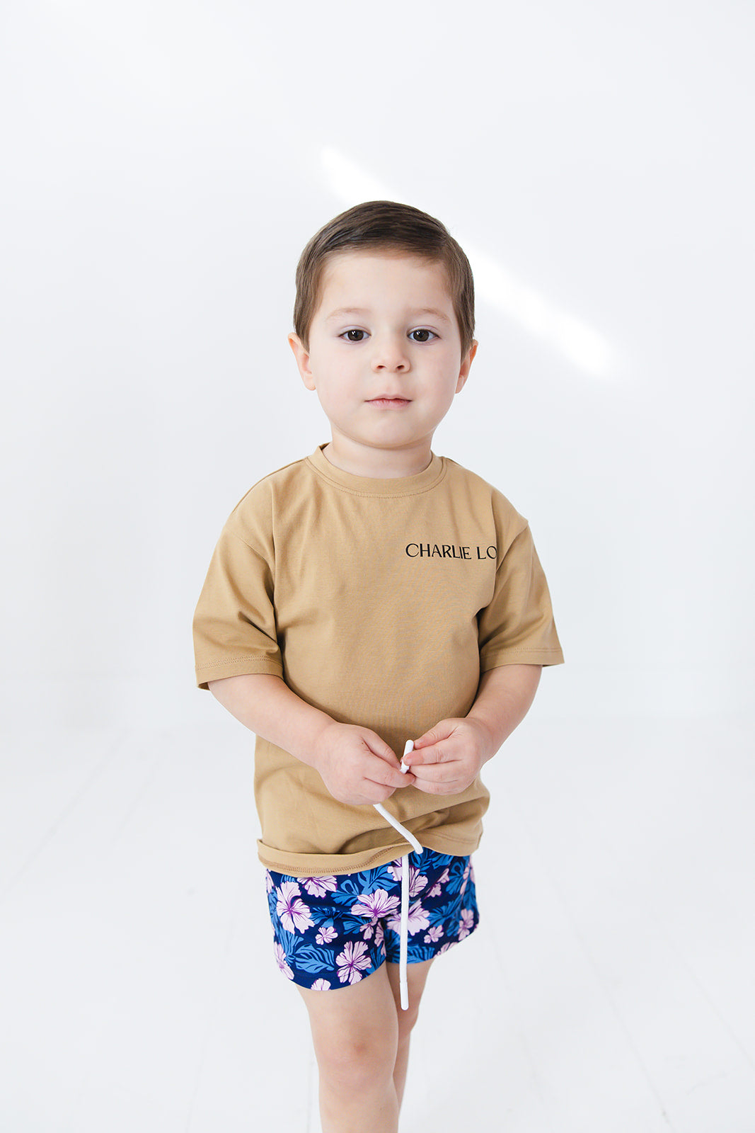 Skater style t-shirt for baby, toddler and little boys. Beige cotton shirt with a truck and palm tree graphic on the back. Soft, stretchy and thick fabric that is perfect for play with Charlie Lou Baby word logo on front.