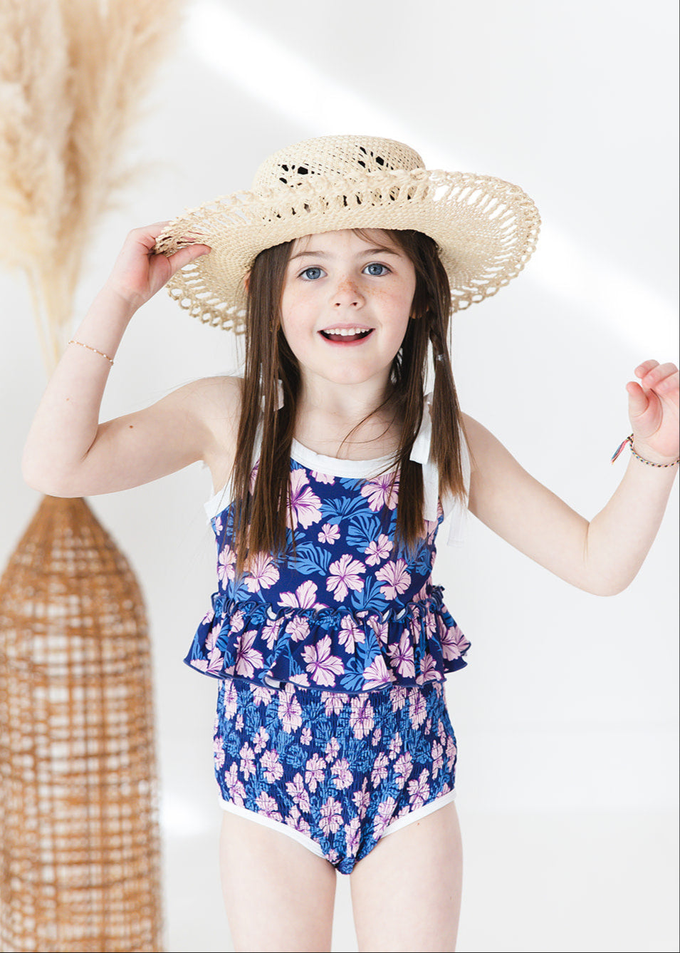 Bathing suit for baby, toddler and little girls. One piece swim suit with pink florals and blue background that is ribbed fabric on the top and smocked on the bottom with adjustable straps that tie into bows.