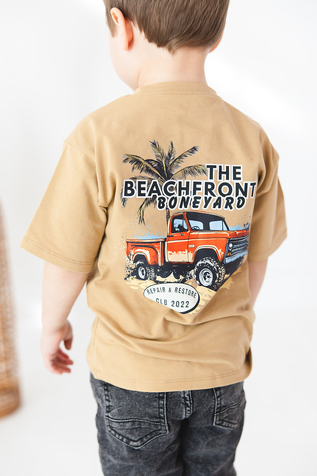 Skater style t-shirt for baby, toddler and little boys. Beige cotton shirt with a truck and palm tree graphic on the back. Soft, stretchy and thick fabric that is perfect for play with Charlie Lou Baby word logo on front.