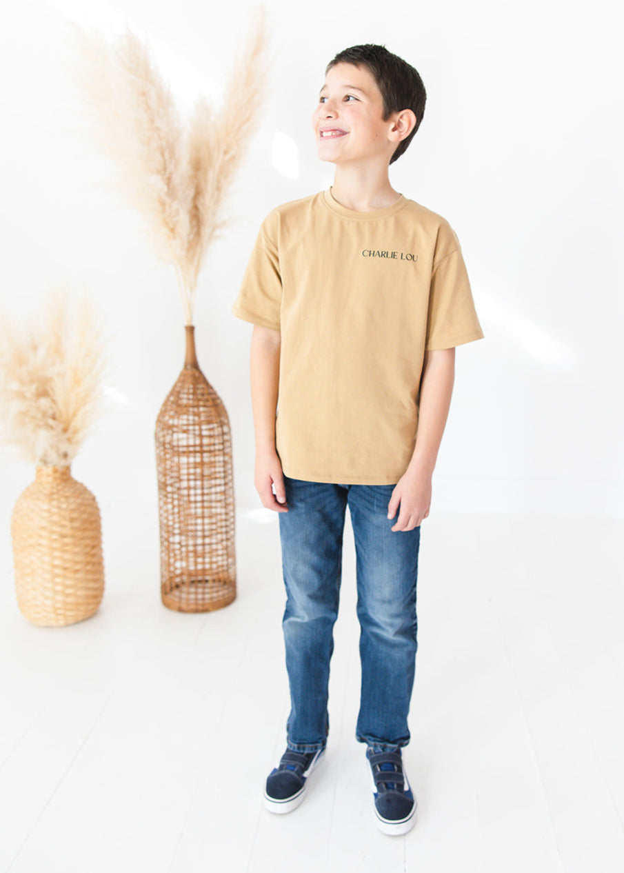 Skater style t-shirt for baby, toddler and little boys. Beige cotton shirt with a truck and palm tree graphic on the back. Soft, stretchy and thick fabric that is perfect for play with Charlie Lou Baby word logo on front.