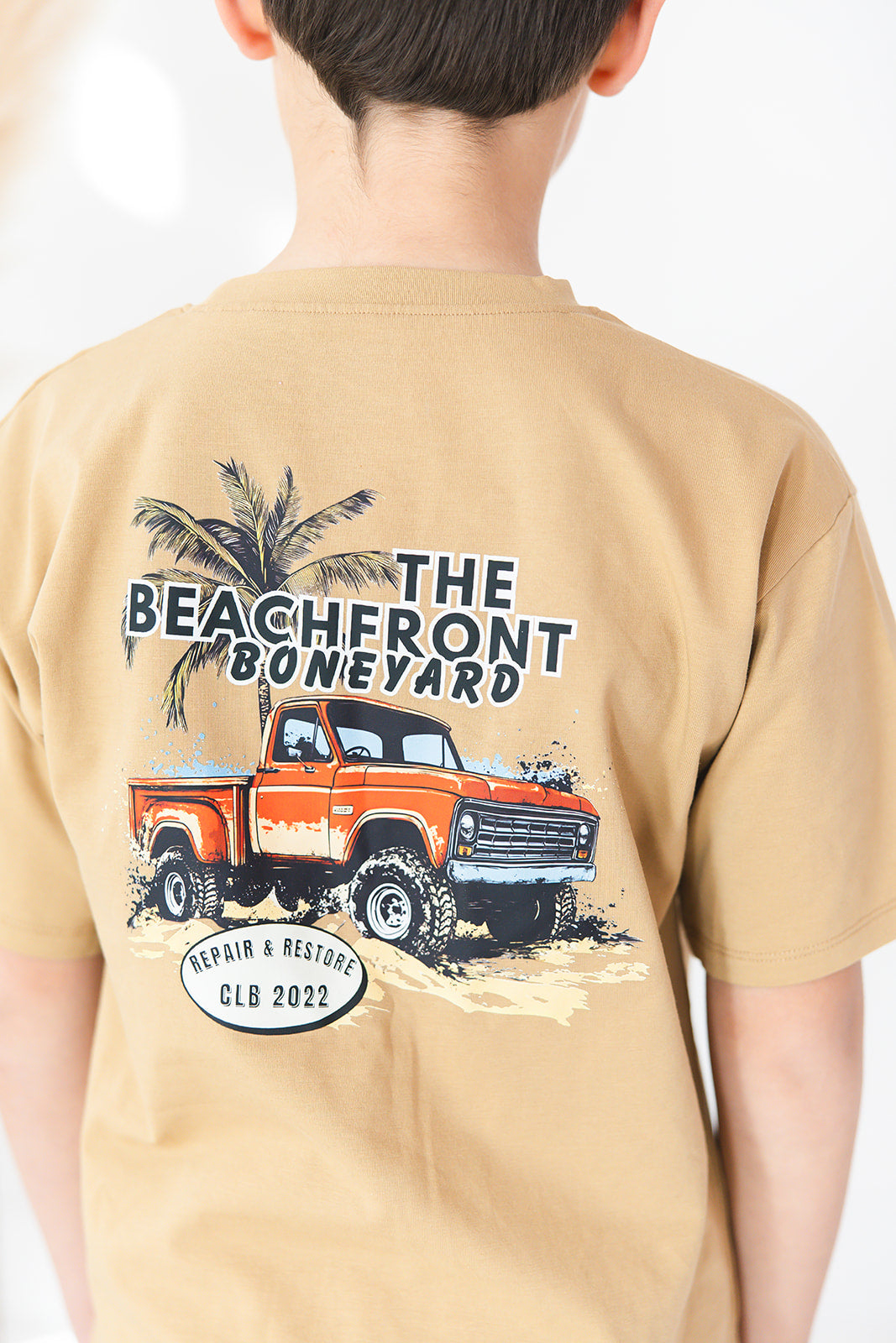 Skater style t-shirt for baby, toddler and little boys. Beige cotton shirt with a truck and palm tree graphic on the back. Soft, stretchy and thick fabric that is perfect for play with Charlie Lou Baby word logo on front.