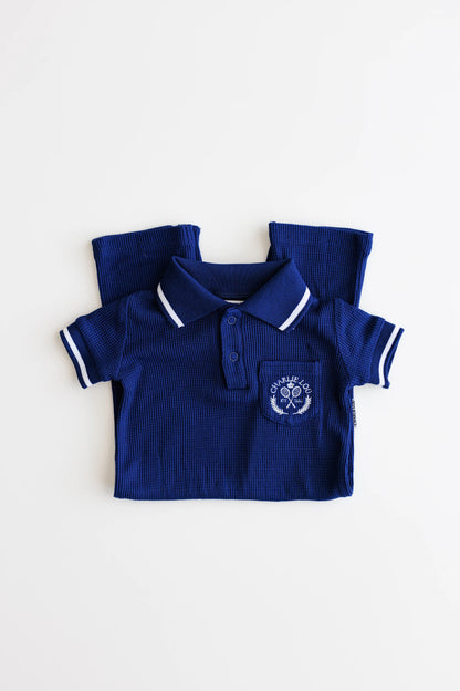 Preppy boys short sleeve polo romper with crotch snaps made from blue waffle bamboo & embroidered with Charlie Lou Baby Club.