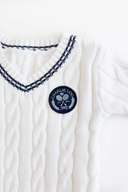 Gender neutral varsity sweater romper in cream and navy blue colors made from chain knit cotton for baby boys and baby girls as well as toddlers.