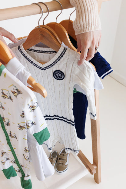 Gender neutral varsity sweater romper in cream and navy blue colors made from chain knit cotton for baby boys and baby girls as well as toddlers.