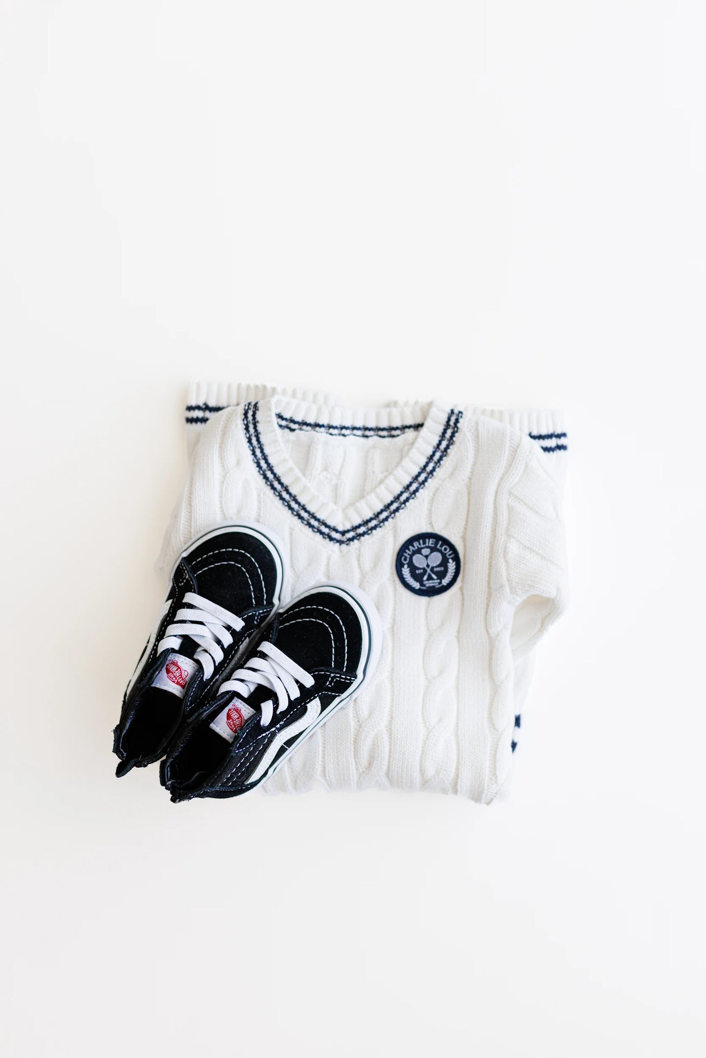 Gender neutral varsity sweater romper in cream and navy blue colors made from chain knit cotton for baby boys and baby girls as well as toddlers.
