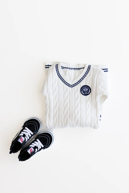 Gender neutral varsity sweater romper in cream and navy blue colors made from chain knit cotton for baby boys and baby girls as well as toddlers.