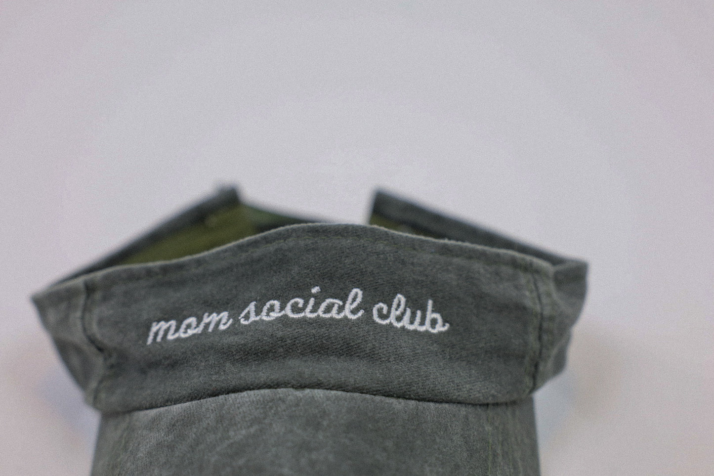 Washed and vintage style visor which is green with words mom social club on it.