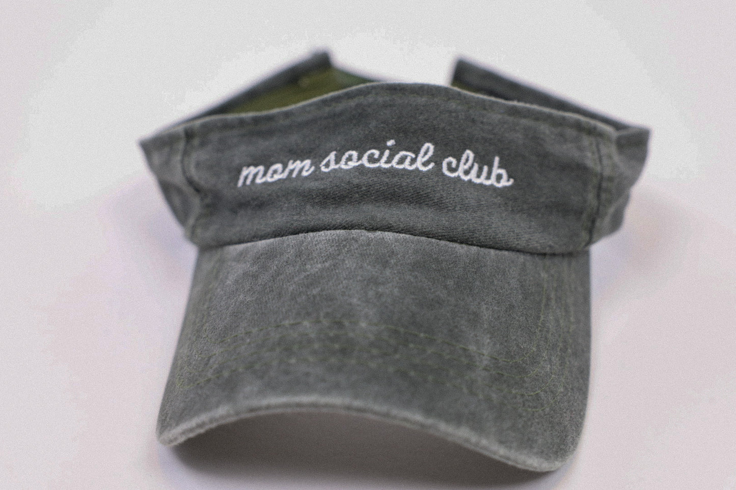Washed and vintage style visor which is green with words mom social club on it.