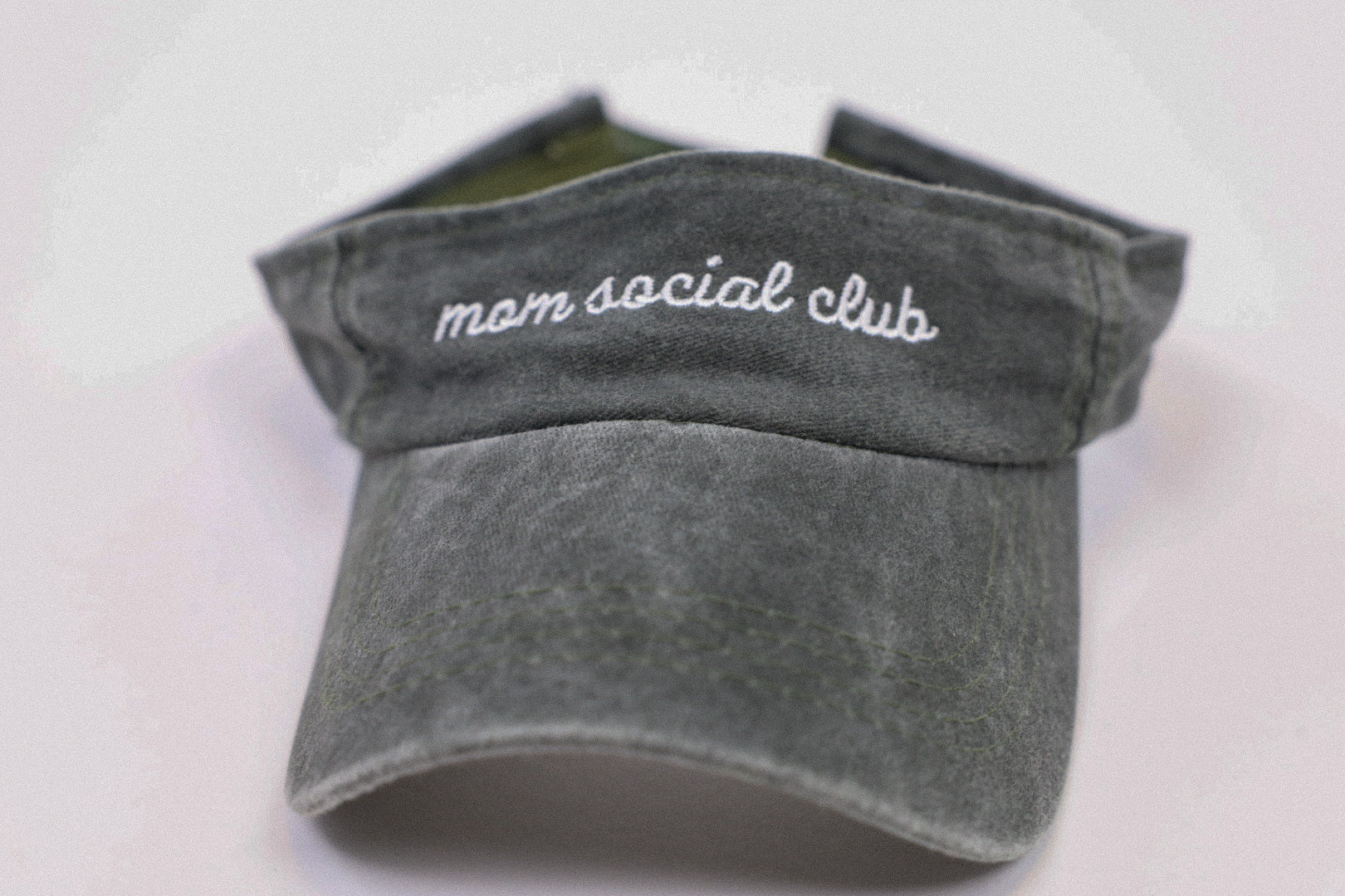 Washed and vintage style visor which is green with words mom social club on it.