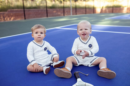 Gender neutral varsity sweater romper in cream and navy blue colors made from chain knit cotton for baby boys and baby girls as well as toddlers.