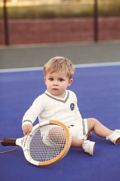 Gender neutral varsity sweater romper in cream and navy blue colors made from chain knit cotton for baby boys and baby girls as well as toddlers.