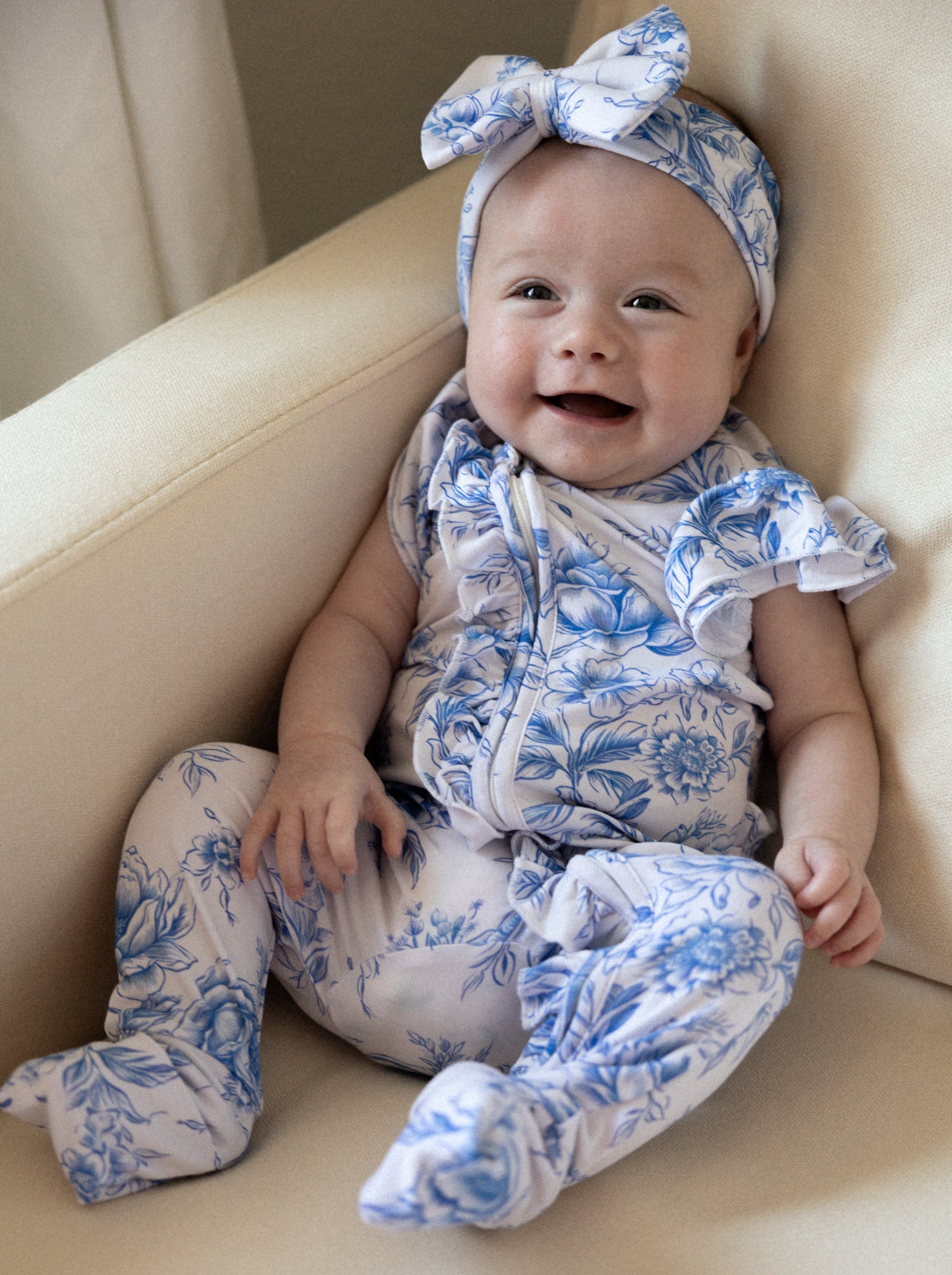 Baby girl wearing blue floral toile bamboo pajamas with ruffles and bamboo bow.