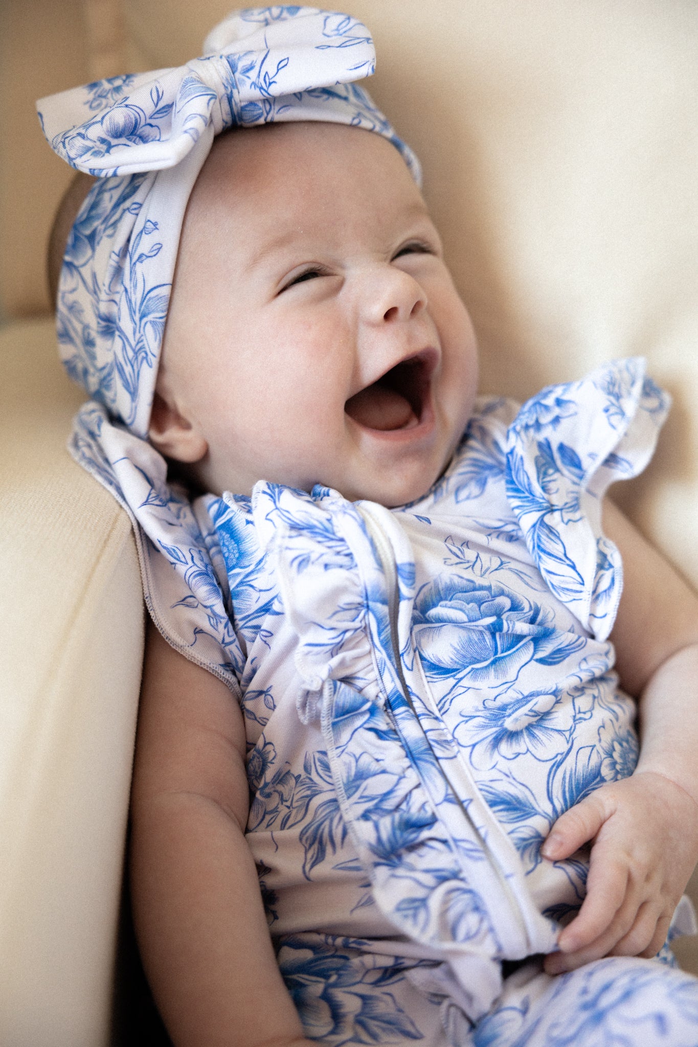 Baby girl wearing blue floral toile bamboo pajamas with ruffles and bamboo bow.