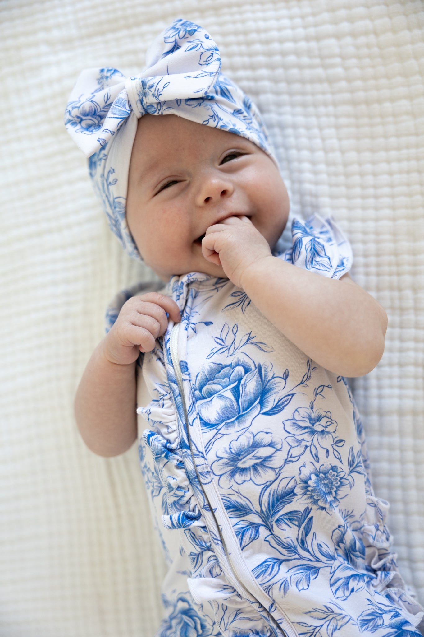 Baby girl wearing blue floral toile bamboo pajamas with ruffles and bamboo bow.